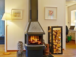 A room with a wood-burning stove, a stack of firewood, and two framed artworks on the wall. - Holiday Home in VÃ¤tÃ¶ (Vätö)
