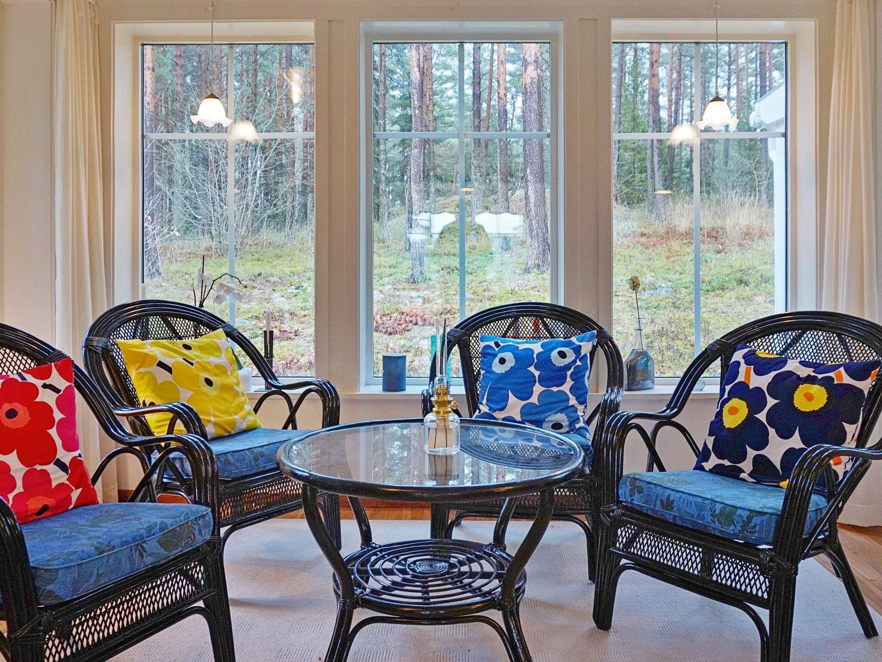 A room with three wicker chairs, a glass table, and large windows with a forest view.