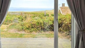 A room with a large window, a wooden deck, and a view of the sea and vegetation. - Holiday Home in Løkken (Lokken)