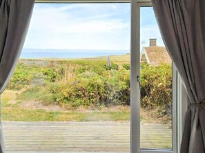 A room with a large window, a wooden deck, and a view of the sea and vegetation. - Holiday Home in Løkken (Lokken)