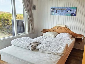 A bed with a wooden headboard, white bedding, and a window with curtains.