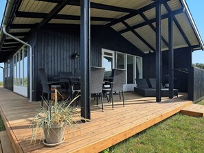 A covered outdoor seating area with a wooden deck, a table, and chairs.