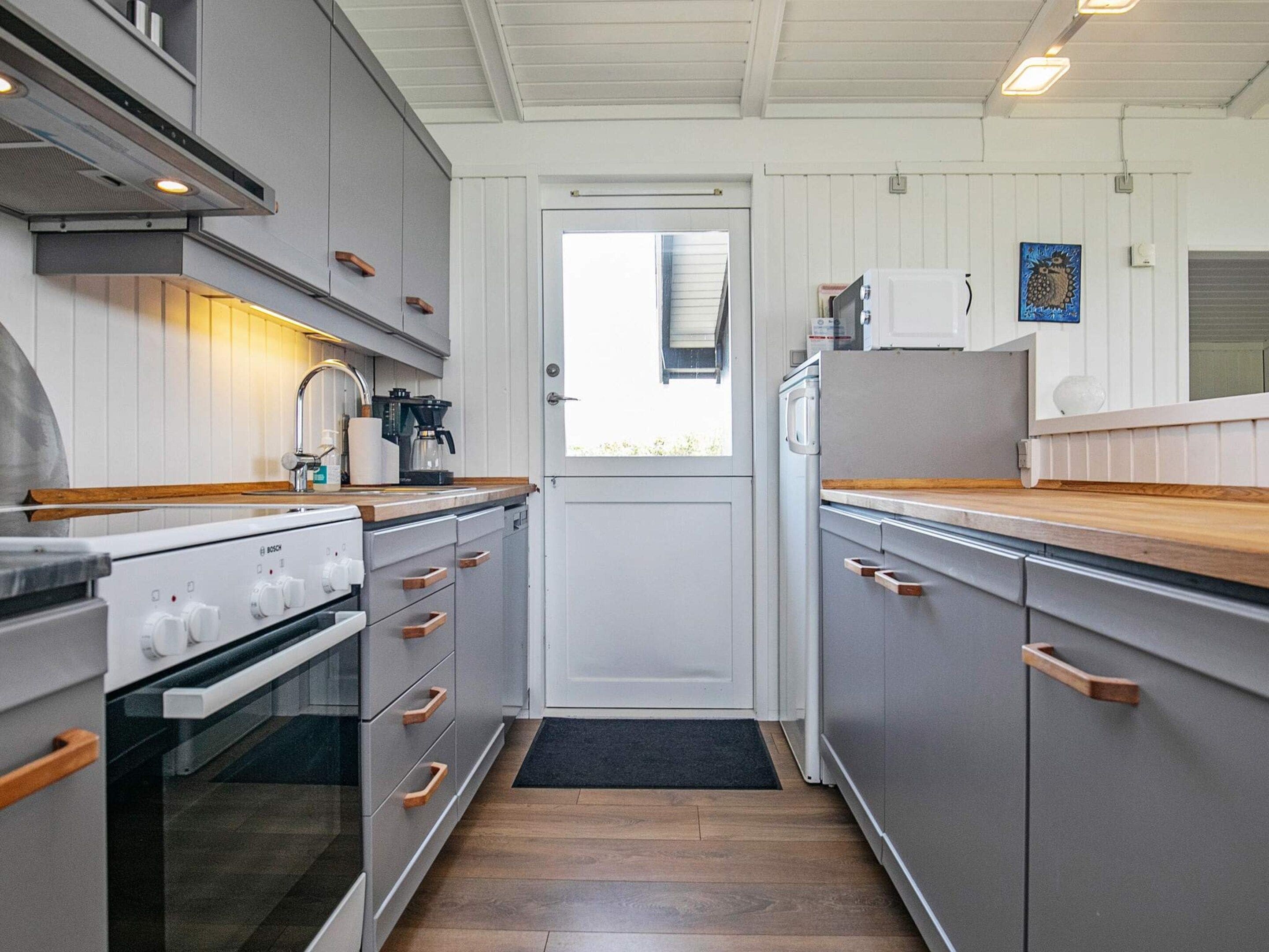 Une cuisine moderne avec des meubles gris, des plans de travail en bois, une cuisinière Bosch et un réfrigérateur.