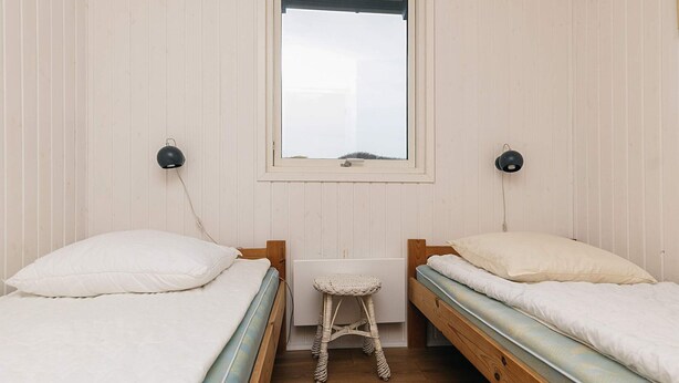 A small, single-room accommodation with two single beds, a small table, and a window. - Holiday Home in Løkken (Lokken)