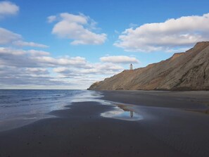 A beach with a lighthouse on a cliff, calm water, and a clear sky.
