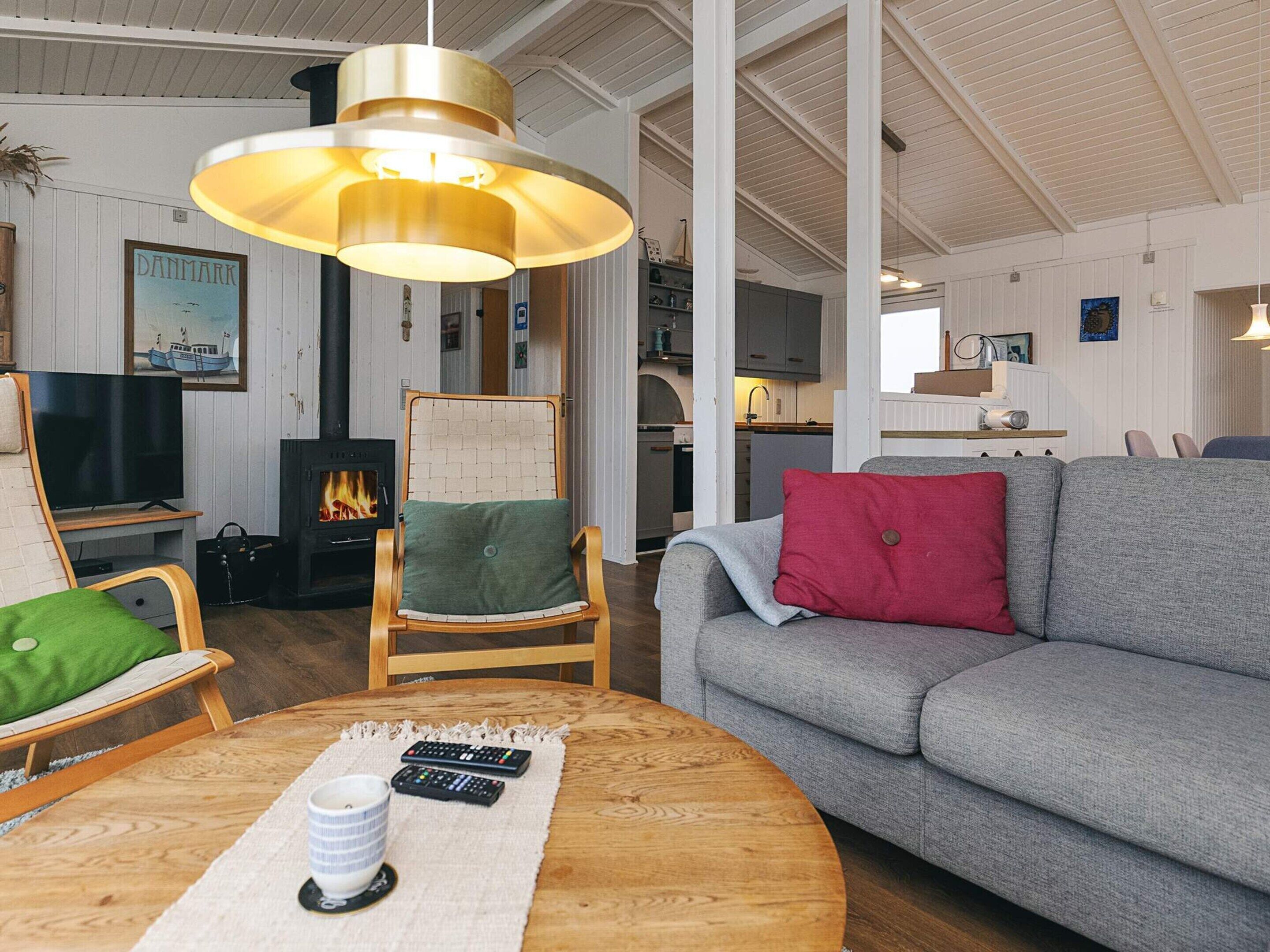 A cozy living room with a fireplace, a sofa, a chair, a television, and a table with remote controls and a mug.