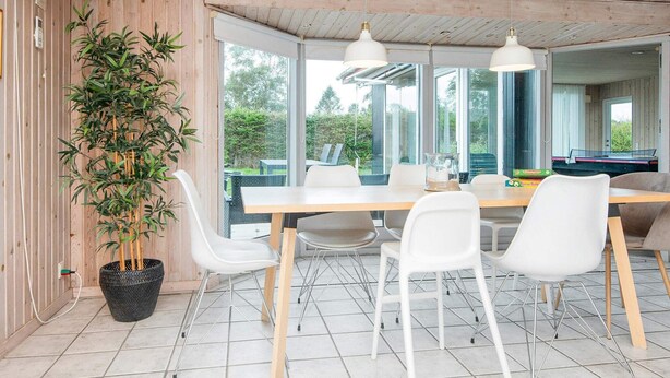 A modern dining area with a wooden ceiling, white chairs, a large table, and a potted plant. - 8 Person Holiday Home in Borkop (Borkop)