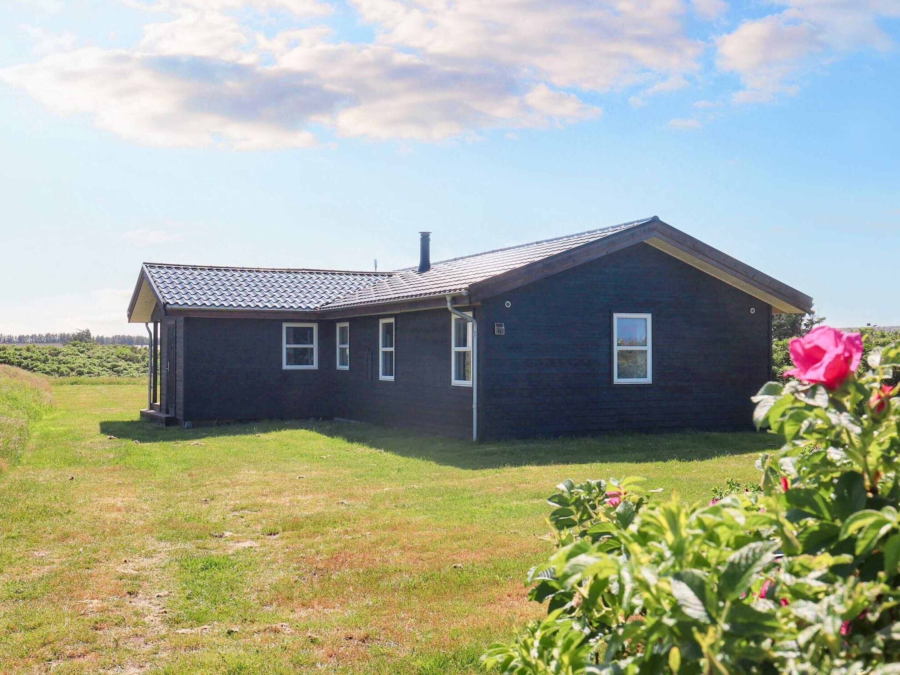 Une maison de plain-pied avec un toit en pente, un porche à l’avant et un petit jardin agrémenté d’un rosier.