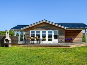 A wooden cabin with a covered patio, a barbecue area, and a view of the surrounding greenery. - 6 Person Holiday Home in Lokken (Lokken)