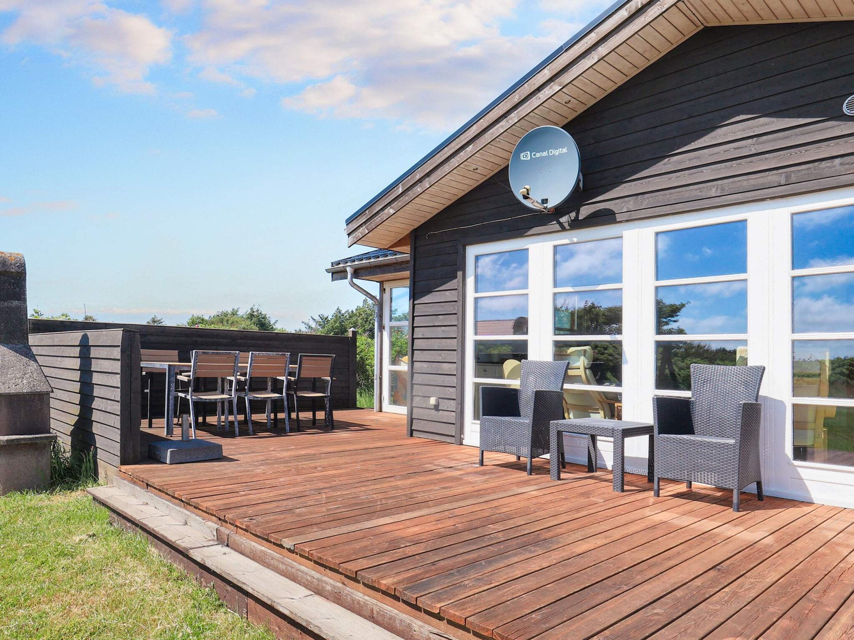 A wooden deck with outdoor furniture, a satellite dish, and a large windowed door.