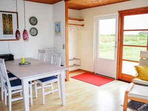 A dining area with a table, chairs, a radio, and a candle. There is a door leading outside with a view of greenery. - 6 Person Holiday Home in Lokken (Lokken)