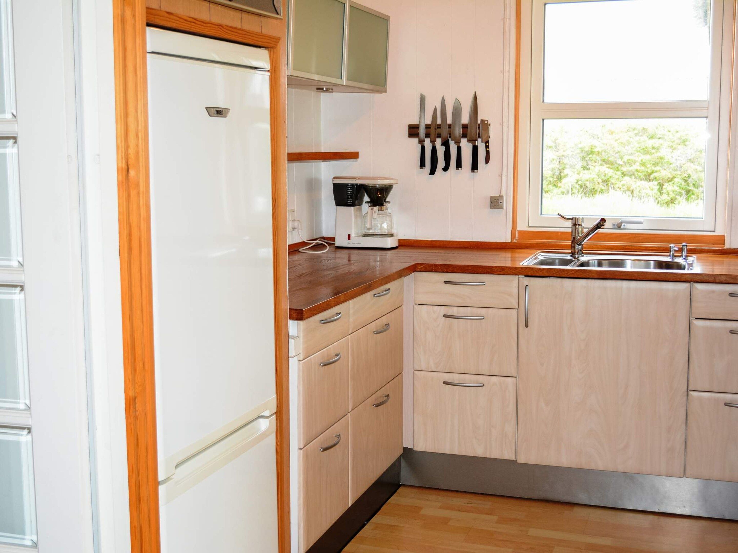 A kitchen with wooden cabinets, a refrigerator, a coffee maker, and a window with a view of greenery.