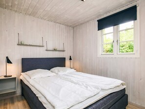 A bedroom with a bed, bedside lamps, a window with a view, and wooden walls.