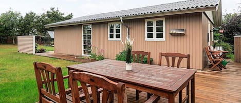 A wooden deck with a table and chairs, a small shed, and a house with a metal roof.