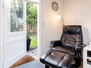 A room with a leather recliner chair, a wall clock, and a door leading to a garden. - 6 Person Holiday Home in Blokhus (Blokhus)