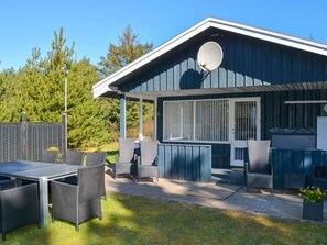 Un espace extérieur abrité, aménagé avec des meubles en osier et doté d’une antenne parabolique fixée sur le bâtiment.