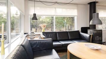 A modern living room with a black leather sofa, a wooden coffee table, and a black wood-burning stove.