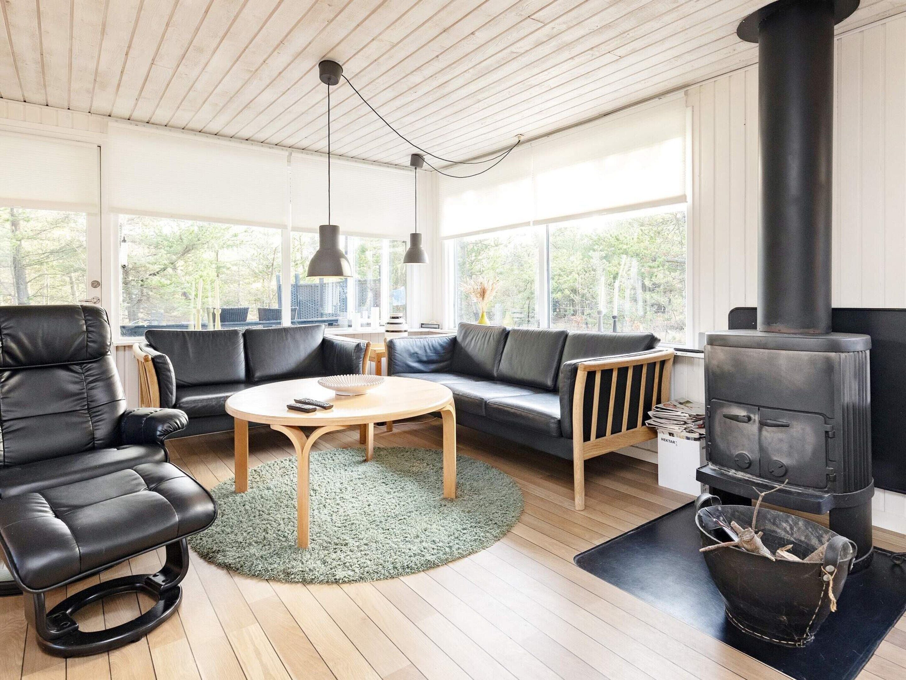 A modern living room with a black leather sofa, a round wooden coffee table, and a black wood-burning stove.