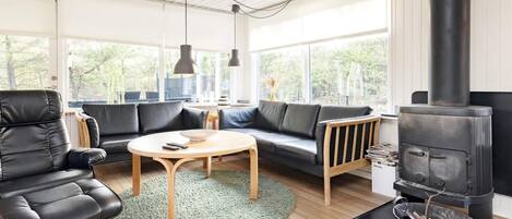 A modern living room with a black leather sofa, a round wooden coffee table, and a black wood-burning stove.