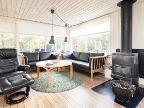 A modern living room with a black leather sofa, a round wooden coffee table, and a black wood-burning stove. - 6 Person Holiday Home in Blokhus (Blokhus)