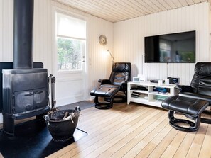 Una sala de estar con estufa de leña, sillones de cuero, televisor de pantalla plana y una estantería.