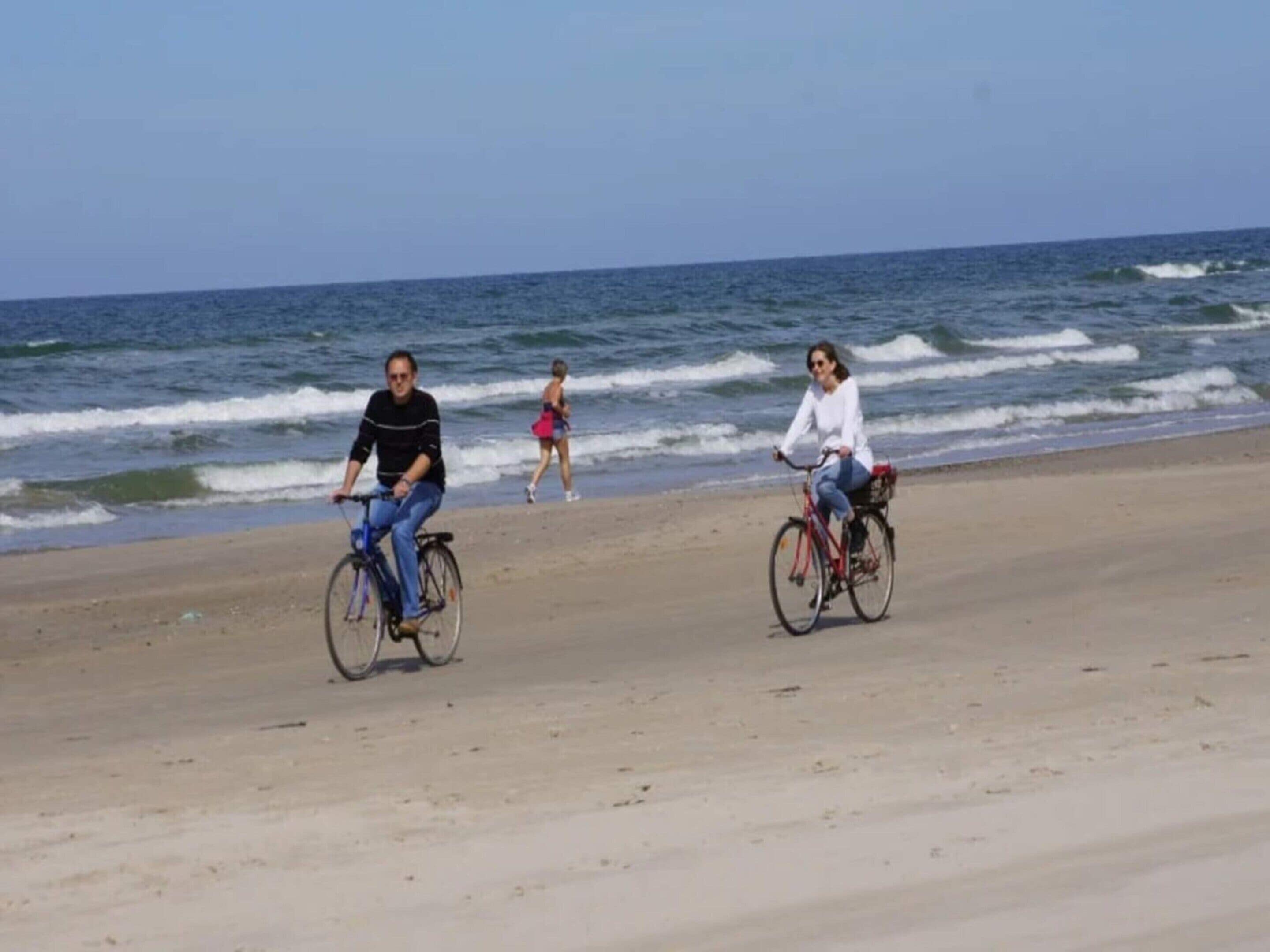 Una playa con dos ciclistas y un peatón al fondo.