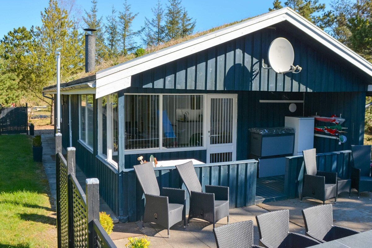Ein kleines, eingeschossiges Gebäude mit einer überdachten Terrasse und Sitzgelegenheiten im Freien.