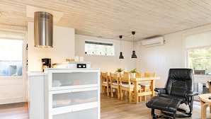 A modern kitchen with a white cabinet, wooden dining table, and chairs, and a black leather chair. - 6 Person Holiday Home in Blokhus (Blokhus)