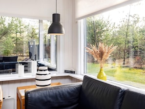 Un interior moderno con un sofá de cuero negro, una mesa blanca con velas y un jarrón amarillo con plantas secas.