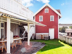 Ein rotes Haus mit einer Holzterrasse und einem überdachten Bereich mit Tisch und Stühlen.