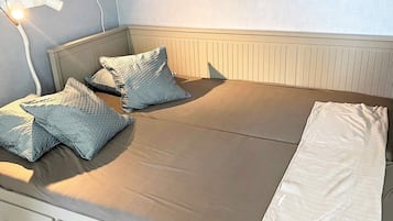 A single bed with a white mattress, two patterned pillows, and a white blanket.