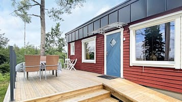A red cabin with a wooden deck, a blue door, and a window overlooking a forest.