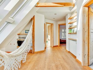 Un pasillo amplio con suelo de madera, una hamaca y vistas a una habitación con ventana.