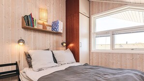 A bedroom with a bed, a wooden shelf with books, a lamp, and a window. - Holiday Home in Jægerspris (Jægerspris)