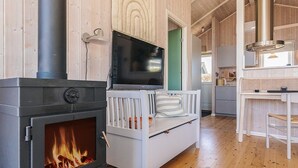 A modern interior with a wood-burning stove, a white sofa with striped pillows, and a television mounted above it. - Holiday Home in Jægerspris (Jægerspris)