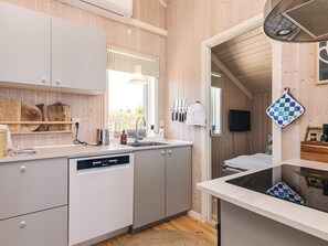 A modern kitchen with wooden walls, a dishwasher, and a window with blinds. - Holiday Home in Jægerspris (Jægerspris)