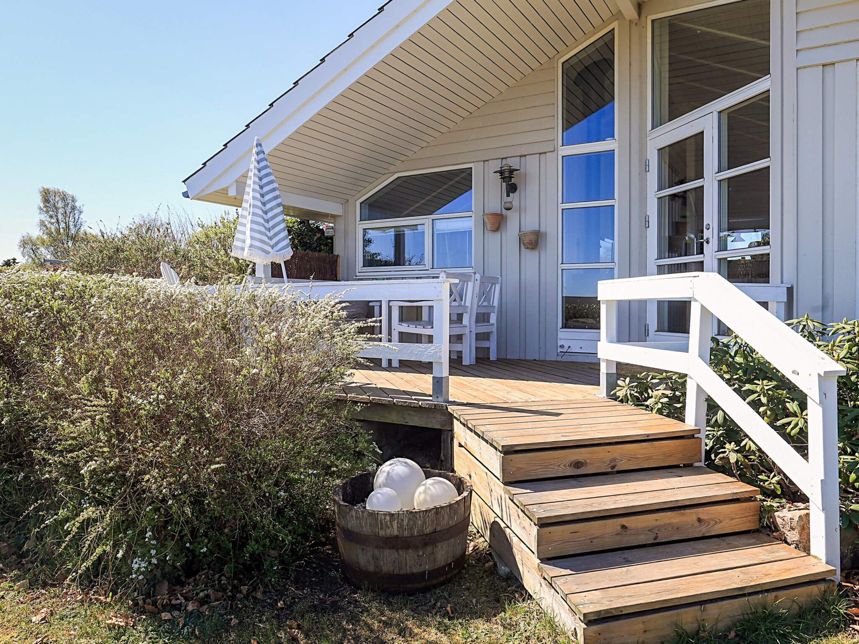 A wooden deck leading to a white building with large windows and a covered porch area.