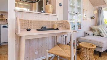Um quarto acolhedor com decoração em madeira, uma mesa de jantar com uma cadeira de fibra natural, um sofá e um armário com portas de vidro.