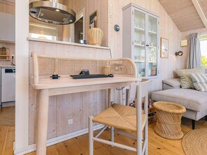 A cozy room with a wooden interior, a dining table with a woven chair, a sofa, and a cabinet with glass doors. - Holiday Home in Jægerspris (Jægerspris)