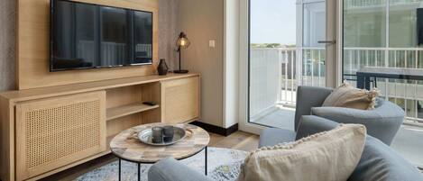 Un salon moderne avec un téléviseur à écran plat, une console en bois, une table basse ronde et des canapés gris.