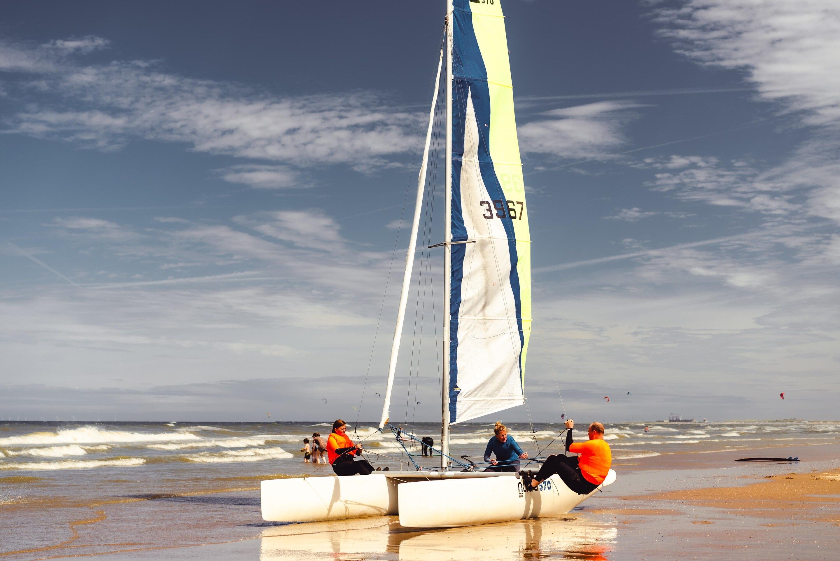 Eine Segelyacht mit zwei Personen an Bord, vor Anker in der Nähe eines Strandes mit Wellen.