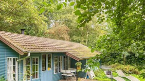 A blue house with a wooden deck, a small patio table, and a chair. - 4 Person Holiday Home in Haderslev (Haderslev)