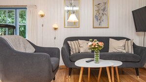 A modern living room with a grey sofa, a matching armchair, a small white coffee table, and a vase of flowers. There are wall-mounted lamps and framed artwork above the sofa. - 4 Person Holiday Home in Haderslev (Haderslev)