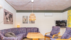 Une pièce comprenant un canapé d’angle, une petite table, deux fauteuils, un téléviseur et des œuvres d’art accrochées aux murs.