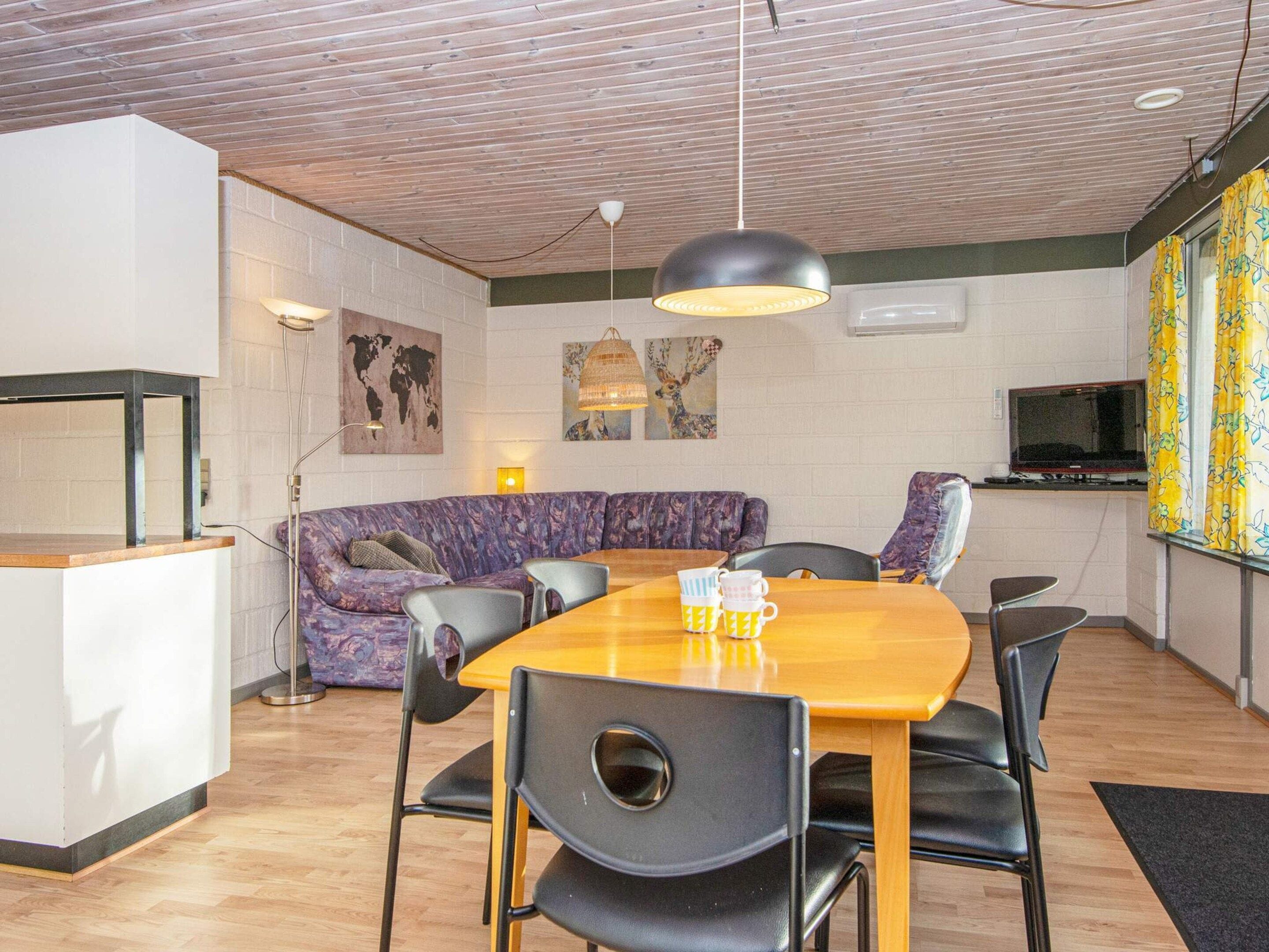Un espacio habitable moderno con techo de madera, un sofá, una mesa de comedor con sillas y un televisor.