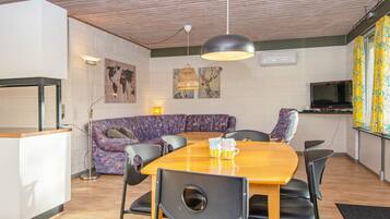 Un espacio habitable moderno con techo de madera, un sofá, una mesa de comedor con sillas y un televisor.