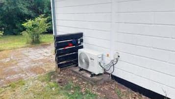 Una unidad de aire acondicionado exterior montada en una pared, un enchufe y una manguera conectada a la unidad.