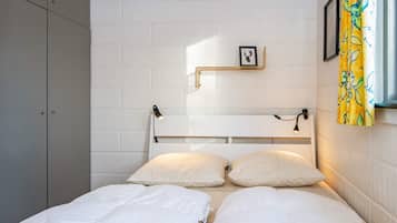 Una habitación con dos camas, un muro de ladrillo blanco, un marco de cuadro y una cortina amarilla.