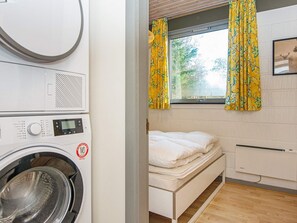 A compact room with a washing machine, a bed, and a window with curtains. - 6 Person Holiday Home in Ans By (Farvang)
