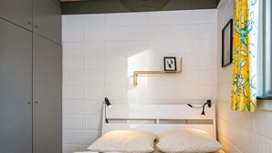 Une pièce avec deux lits, un mur en briques blanches, un cadre photo et un rideau jaune.